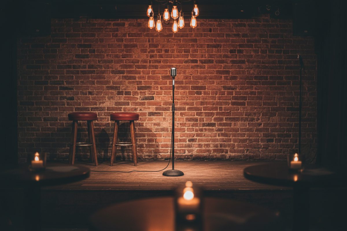 Empty comedy club interior with brick wall, low stage, and microphone